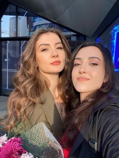 two women taking a selfie in front of a building with blue lights and flowers