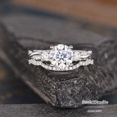 an engagement ring with three stone settings on top of a piece of black rock in front of a wooden background