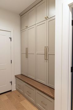 an empty walk in closet next to a white door and wooden bench with drawers on both sides