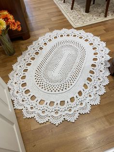 a white doily sitting on top of a wooden floor next to a vase with flowers