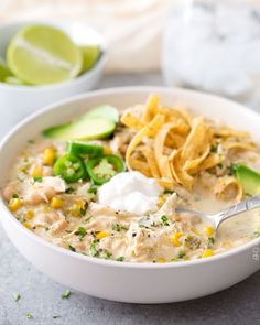 a white bowl filled with chicken tortilla soup and topped with sour cream, avocado chips