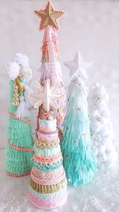 three small christmas trees are decorated in pastel colors and fringes with stars on top