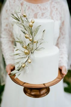 a close up of a person holding a white cake with gold decorations on the top