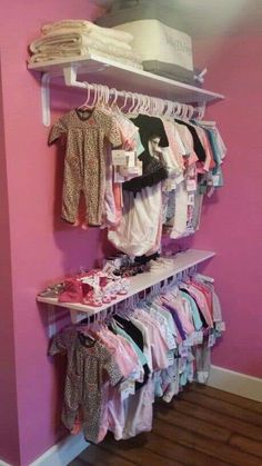 a baby's clothing rack in the corner of a room with pink walls and wooden floors