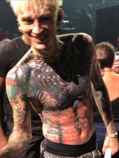 a man with lots of tattoos on his chest and arm is standing in front of a crowd