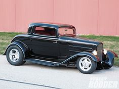 an old model black car parked on the side of the road in front of a red building