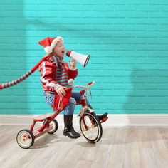 a young boy riding a tricycle with a megaphone in his mouth and wearing a santa hat