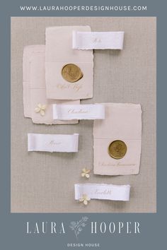 four pieces of white paper with gold buttons and name tags attached to them, sitting on top of each other