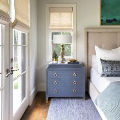 a bedroom with a blue dresser next to a bed and two windows in the room