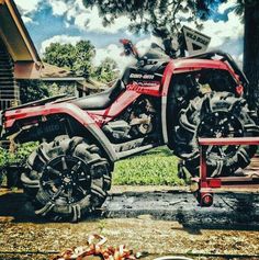 a red and black four - wheeler parked in front of a house next to a tree