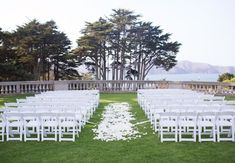 an outdoor ceremony setup with white chairs and petals on the grass