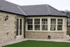 a stone house with white windows and green grass