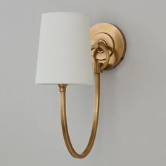 a gold wall light with a white shade on the side and a lamp attached to it