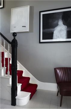 a red chair sitting in front of a white stair case next to a painting on the wall