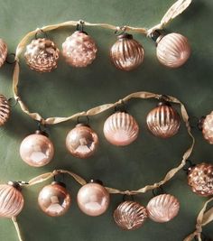 some pink ornaments are hanging on a green tablecloth with ribbon around them and one is decorated with seashells