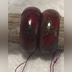 two red apples sitting on top of a piece of wood next to some thread and a wooden stick