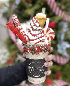 a person holding up a cup filled with candy canes and marshmallows