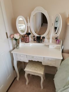 a white vanity with three round mirrors on it's sides and two stools