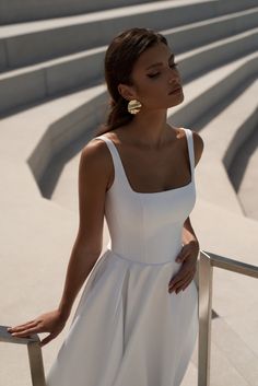 a woman in a white dress leaning against a railing with her hands on her hips