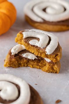 two pumpkin cinnamon rolls with frosting on top and one in the foreground next to an orange pumpkin