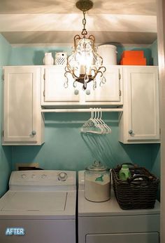 a washer and dryer in a small room with blue walls, white cabinets and a chandelier hanging from the ceiling