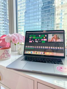 an open laptop computer sitting on top of a white desk next to flowers and vases