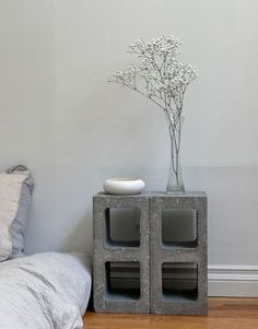 a vase with flowers sitting on top of a cement block next to a bed in a bedroom