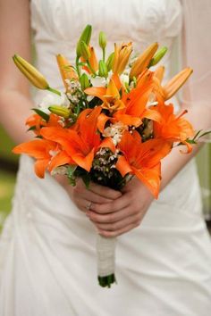 a bride holding a bouquet of orange lilies and white orchids in her hand