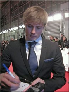 a man in a suit and tie writing on a notepad while holding a cell phone