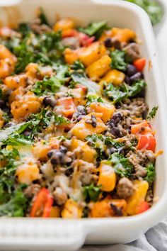 a white casserole dish filled with vegetables and black beans, topped with cheese