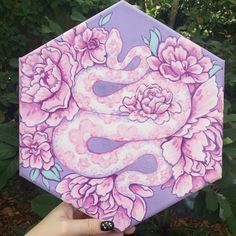 a hand holding up a painted hexagonal object in front of some plants and flowers