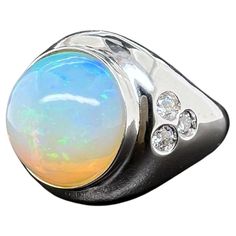 This stunning Ethiopian opal men's ring is a must have for any collection. The round opal glows with green, blue and yellow hues. The diamonds are inlayed on the sides to give a nice accent to the sleek ring. The overall design of the ring is made to be worn comfortably and will not catch on apparel. Ring Size: 12.75 (can be sized) Diamonds 0.58 ct. Round Brilliant Ethiopian Opal: 11.20 cts, Round Cabochon Metal: 14k White Gold Ethiopian Opal Multi-stone Ring, Modern Round Opal Ring, Opal White, Domed Ring, Ethiopian Opal, Round Brilliant, Diamond Rings, Rings For Men, Jewelry Rings