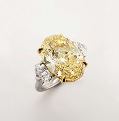 a fancy yellow and white diamond ring with three diamonds on the sides, set in 18k gold