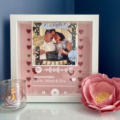 a photo frame with a pink flower next to it and a candle on the table