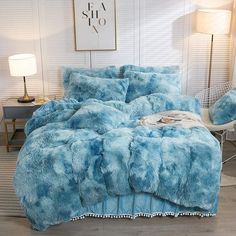 a bed with blue comforters and pillows in a room next to a lamp on a table