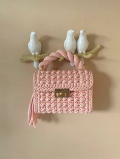 a pink crocheted purse hanging on a wall with two birds perched on it