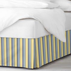 a bed with white sheets and blue and yellow striped bedskirt on the floor