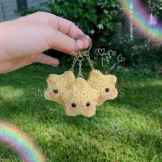 a hand holding a keychain with two little bears on it and a rainbow in the background