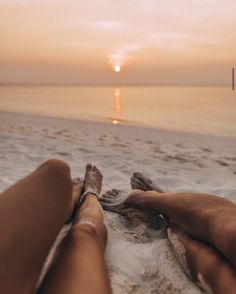 someone is laying down on the beach with their feet up in the sand as the sun sets