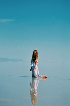 a woman is sitting on the water with her legs spread out and looking at something in the distance