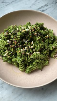 a white plate topped with pasta covered in green sauce and toppings on top of a marble table