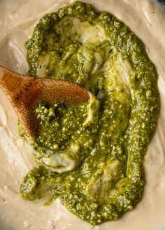 a wooden spoon in a bowl filled with pesto and cheese dips, ready to be mixed together