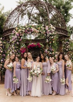 a group of women standing next to each other in front of a gazebo covered with flowers