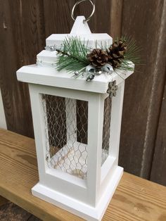 a white birdcage with pine cones and greenery sits on a wooden bench