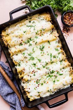 a casserole dish with cheese and herbs on the side next to some seasonings