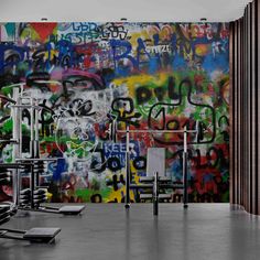 a wall covered in lots of graffiti next to a gym equipment set up on top of a hard wood floor