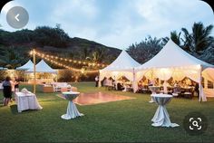 an outdoor event with tables and chairs set up under white tented tents at night