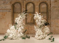 two white flowers sitting on top of each other in front of a stone wall with arched windows