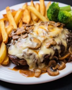 a white plate topped with meat covered in gravy next to fries and broccoli