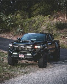 a black truck parked on the side of a road near some grass and trees in the background